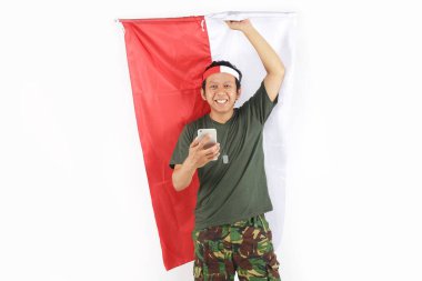 Endonezyalı asker gülümsüyor. Akıllı telefon kullanıyor ve bayrak tutuyor.