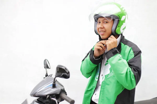 Genç Asyalı adam kaskını ve yeşil ceketini kullanarak motosiklet kullanıyor. 19 Mart 2018. Yogyakarta Endonezya