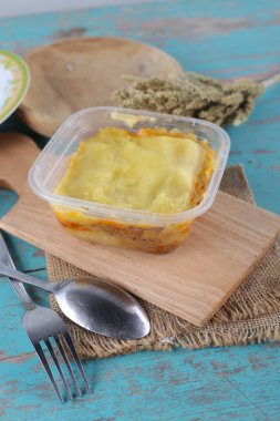 Mavi ahşap masa üzerinde ev yapımı sebzeli plastik konteynır.