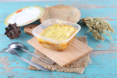 Mavi ahşap masa üzerinde ev yapımı sebzeli plastik konteynır.