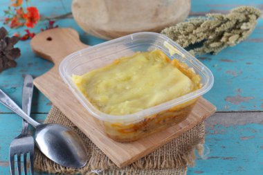 Mavi ahşap masa üzerinde ev yapımı sebzeli plastik konteynır.