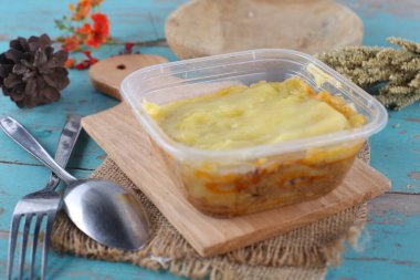 Mavi ahşap masa üzerinde ev yapımı sebzeli plastik konteynır.