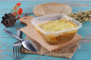 Mavi ahşap masa üzerinde ev yapımı sebzeli plastik konteynır.