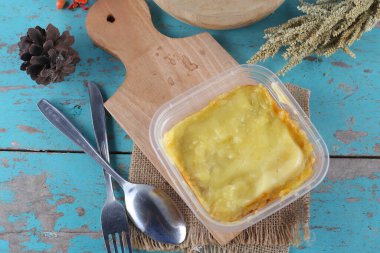 Mavi ahşap masa üzerinde ev yapımı sebzeli plastik konteynır.