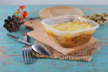 Mavi ahşap masa üzerinde ev yapımı sebzeli plastik konteynır.