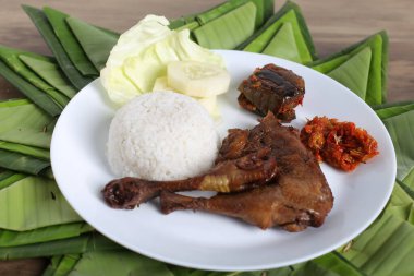 Kızarmış tavuk budu, haşlanmış pirinç ve dilimlenmiş salatalık, ahşap masa arkaplanı.