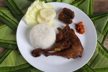 Kızarmış tavuk budu, haşlanmış pirinç ve dilimlenmiş salatalık, ahşap masa arkaplanı.