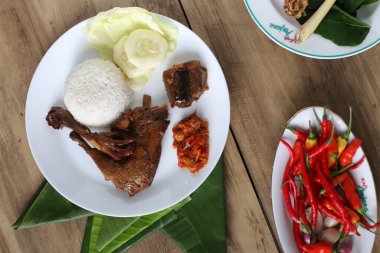 Kızarmış tavuk budu, haşlanmış pirinç ve dilimlenmiş salatalık, ahşap masa arkaplanı.