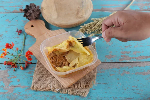 Mavi ahşap masa üzerinde ev yapımı sebzeli plastik konteynır.