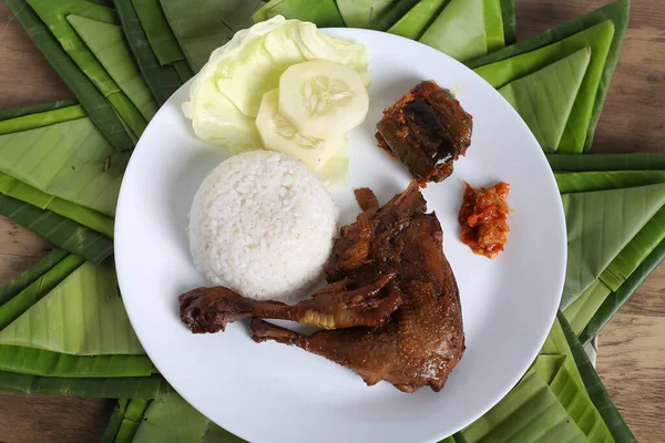 Kızarmış tavuk budu, haşlanmış pirinç ve dilimlenmiş salatalık, ahşap masa arkaplanı.