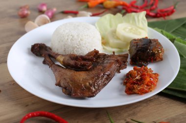 Kızarmış tavuk budu, haşlanmış pirinç ve dilimlenmiş salatalık, ahşap masa arkaplanı.