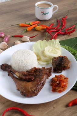 Kızarmış tavuk budu, haşlanmış pirinç ve dilimlenmiş salatalık, ahşap masa arkaplanı.