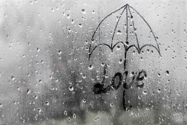 drawing the inscription love under an umbrella on a wet window with copy space