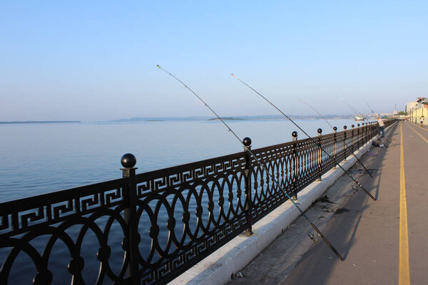 several of fishing rods with coils while fishing on the embankment of the Volga River are leaning against the forged fence in the ornament horizontal