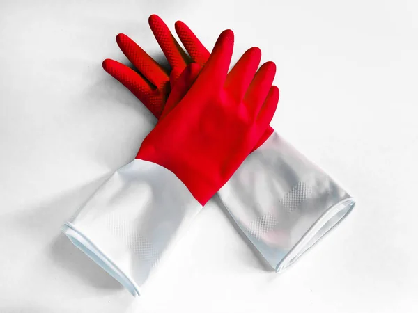 A pair of red rubber gloves lay on a white background for protecting hands on the time for housekeeping, gardening, cleaning, washing the floor, washing dishes, washing windows. commercial cleaning co