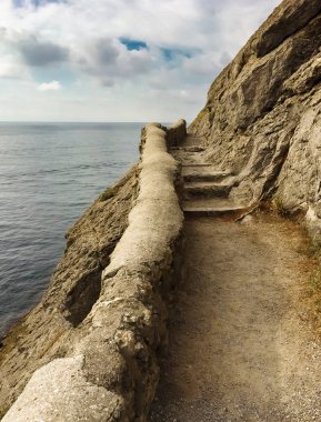 denize ve bulutlara karşı taş basamaklar ile deniz boyunca eski bir taş yolu ile uçurumun kenarı, dikey çerçeve
