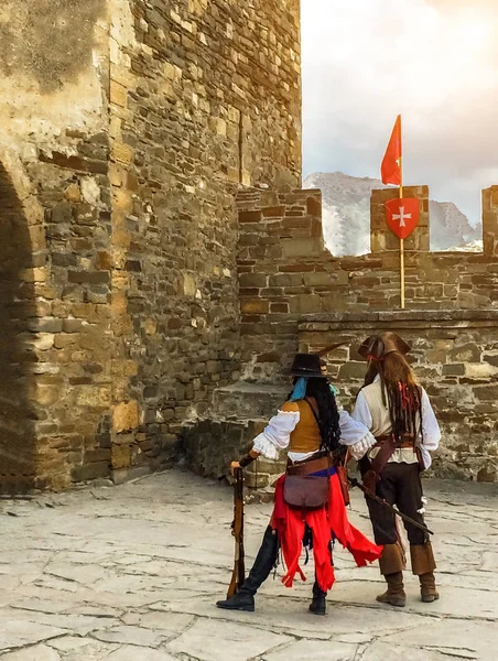 View from the back two characters in the costumes of pirates on the background of the ancient fortress wall, festival Genoese helmet in the Crimea, costume reconstruction of historical events — Stock Photo, Image