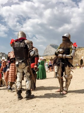 Sudak - 16 Ağustos 2015: Festivalde zırhlı, zırhlı, zırhlı, zırhlı, zırhlı ve miğferli iki ortaçağ şövalyesi, arka planda dağ, kale duvarları ve seyirci kalabalığına karşı durmaktadır.