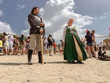 Sudak - 16 Ağustos 2015: Çelik zırhlı zengin bir ortaçağ şövalyesi elinde balta ve yeşil elbiseli genç bir bayan hizmetçi, meydanda, gökyüzüne, kalabalığa ve kaleye karşı, tarihi yeniden canlandıran, yerden bakan