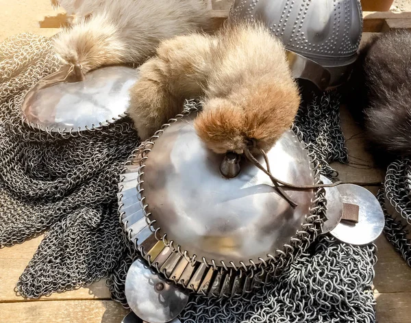 Close-up copy of the ancient shiny helmets with chainmail mesh and fur tails on top lie on a wooden table, top view, antique armor in sun glare — Stock Photo, Image