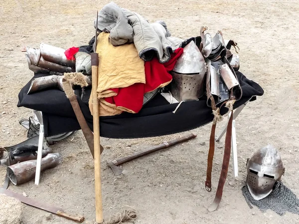 The clothes, armor and weapons of medieval knight lie mountain on felt in the open air. Protective antique helmet, chainmail, battle ax, metal battens, festival reconstruction — Stock Photo, Image