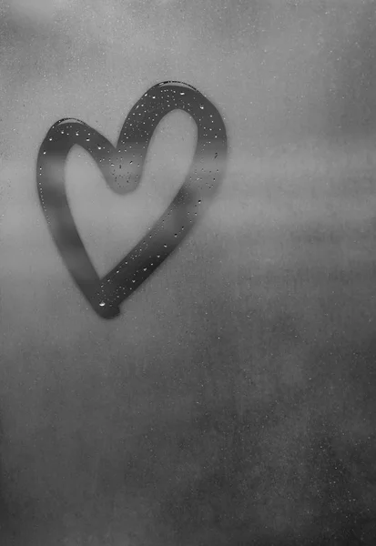 Dark gray heart painted on sweaty glass, there are many drops on it, inscription heart and love using handmade on wet gray autumn foggy glass