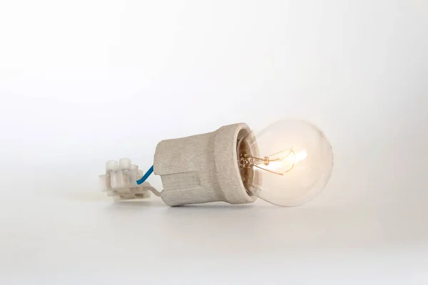 Lighting incandescent lamp bulb with cap, socket, wires and terminal block lies on white background, new idea concept