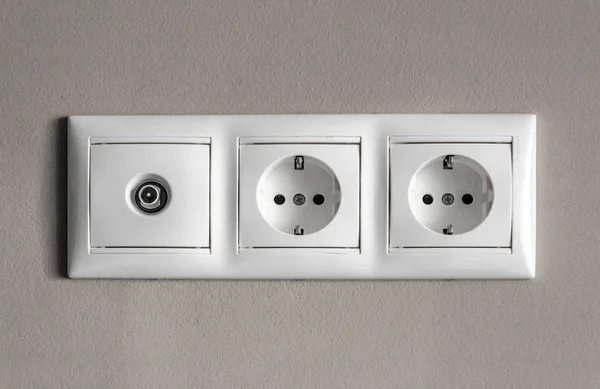 electrical outlets, a set of three white empty electrical sockets and an antenna connector for a TV on an empty gray