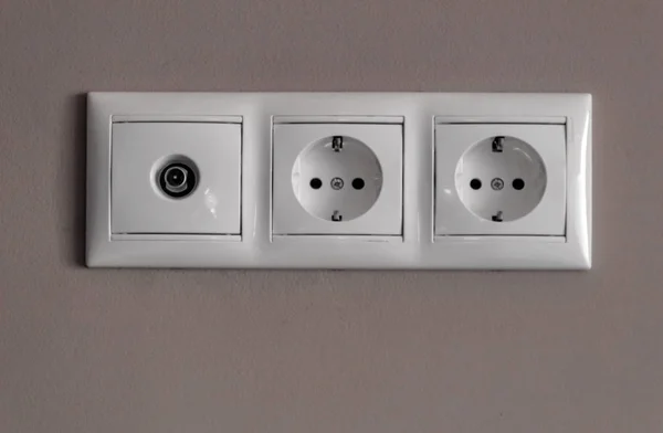 电源插座，一组用于电器的三个白色空电源插座和一个空灰色电视上的电视天线连接器 — 图库照片
