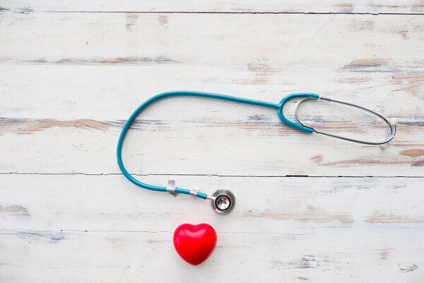 Blue stethoscope with red heart on white wooden background.
