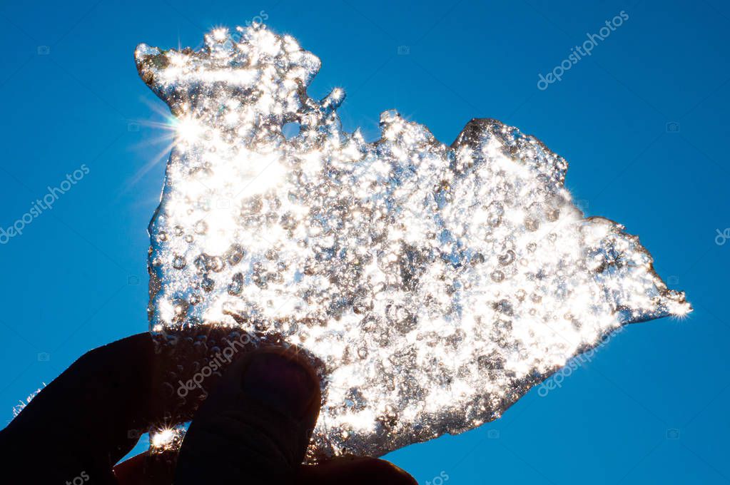 Thin transparent ice in a hand of the person directed on spring sunshine. Beautiful blue sky