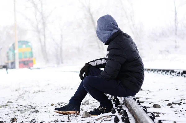 Man sit on railway in front of the train. Boy solitude and sad. Suicide thought. winter