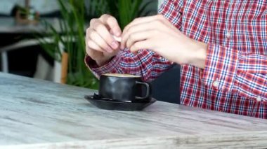 Adam bir kafede oturmuş bir fincan kahve içiyor. Cappuccino. Bir restoran. elinde şeker sopa