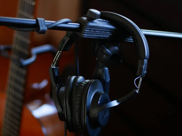 Μαύρα ακουστικά στούντιο σε μια βάση και μαύρο φόντο κιθάρας. — Φωτογραφία Αρχείου