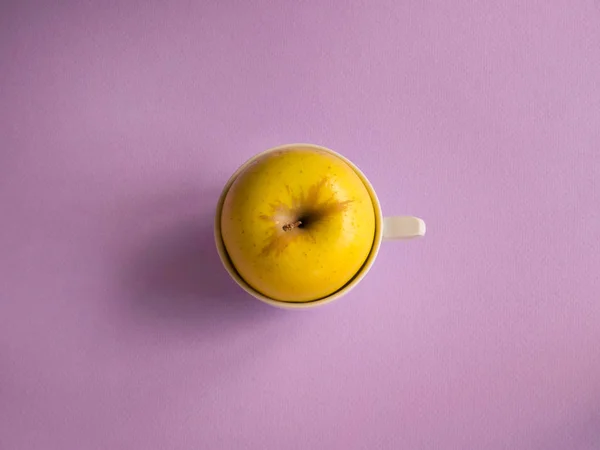 yellow apple in a cup on a pink background top view