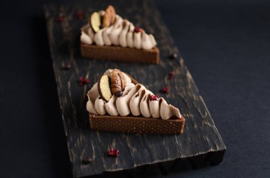 Koyu ahşap arka plan üzerinde ceviz fındık ve küçük çikolata topları ile dekore edilmiş çikolata mini tart