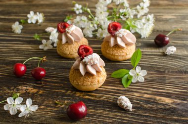 Craquelin ile Choux Buns (gevrek krem puffs) kiraz krem taze kiraz, kiraz çiçekleri ve ahşap arka plan üzerinde badem ile dekore ile dolu