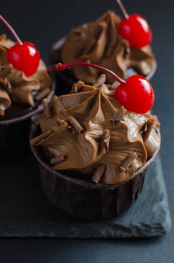 Siyah arka plan üzerinde kokteyl kiraz ile süslenmiş çikolata krema ile Çikolata cupcakes