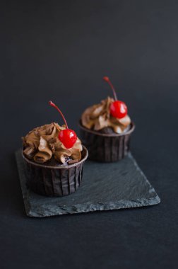Siyah arka plan üzerinde kokteyl kiraz ile süslenmiş çikolata krema ile Çikolata cupcakes