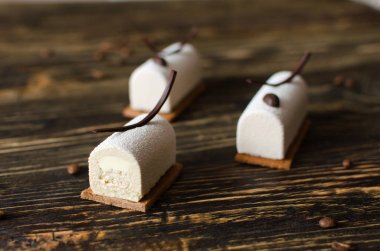 Coffee mini mousse cakes covered with white velvet spray, decorated with coffee beans and chocolate elements on a wooden table