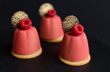 Çikolata elemanları ve siyah arka planda taze ahududu ile süslenmiş pembe kadife sprey ile kaplı çikolata mini Mousse kek seti