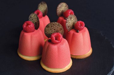 Çikolata elemanları ve siyah arka planda taze ahududu ile süslenmiş pembe kadife sprey ile kaplı çikolata mini Mousse kek seti