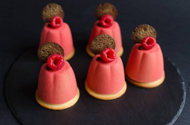 Çikolata elemanları ve siyah arka planda taze ahududu ile süslenmiş pembe kadife sprey ile kaplı çikolata mini Mousse kek seti