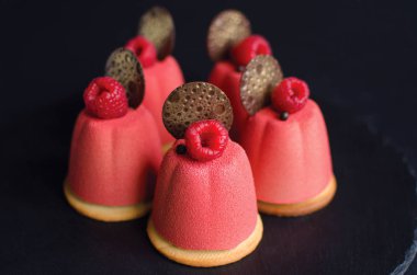 Çikolata elemanları ve siyah arka planda taze ahududu ile süslenmiş pembe kadife sprey ile kaplı çikolata mini Mousse kek seti