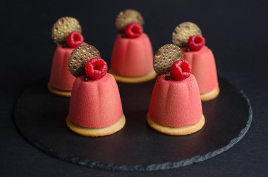 Çikolata elemanları ve siyah arka planda taze ahududu ile süslenmiş pembe kadife sprey ile kaplı çikolata mini Mousse kek seti