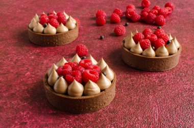 Taze ahududu ve arka planda kırmızı çikolata gevrek topları ile dekore edilmiş çikolata mini tart seti