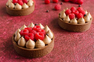 Taze ahududu ve arka planda kırmızı çikolata gevrek topları ile dekore edilmiş çikolata mini tart seti