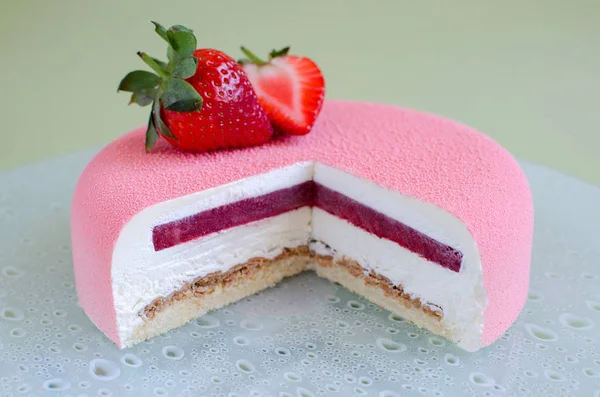 Part of contemporary strawberry mousse cake covered with pink velvet cocoa spray decorated with fresh strawberries on green background