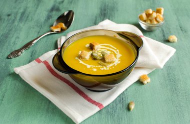 Pumpkin cream soup in a black glass plate on a green background