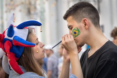 Moskova, Rusya - 23 Haziran 2018: Rus kız hayran Brezilya bayrağı çizim renkli şapka içinde yanak Brezilyalı adam Moskova Nikolskaya Caddesi üzerinde dünya championchip sırasında.